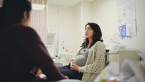 A woman sitting comfortably in her OB-GYN's clinic as she discusses her care with the obstetrician.