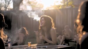 a woman smoking a cigarette in the backyard of her house, joined by her friends